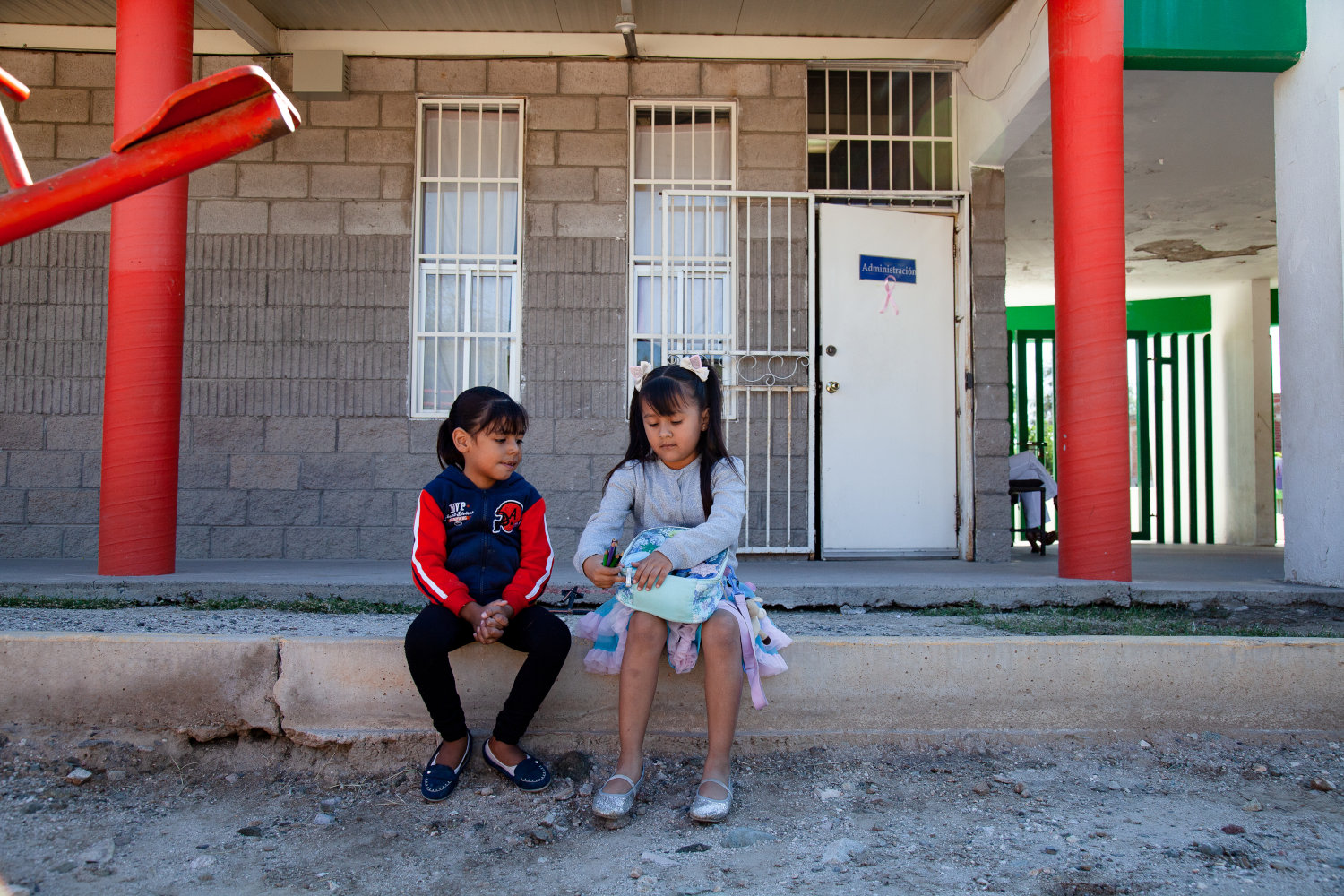 2 niños sentados frente a una escuela con lonchera